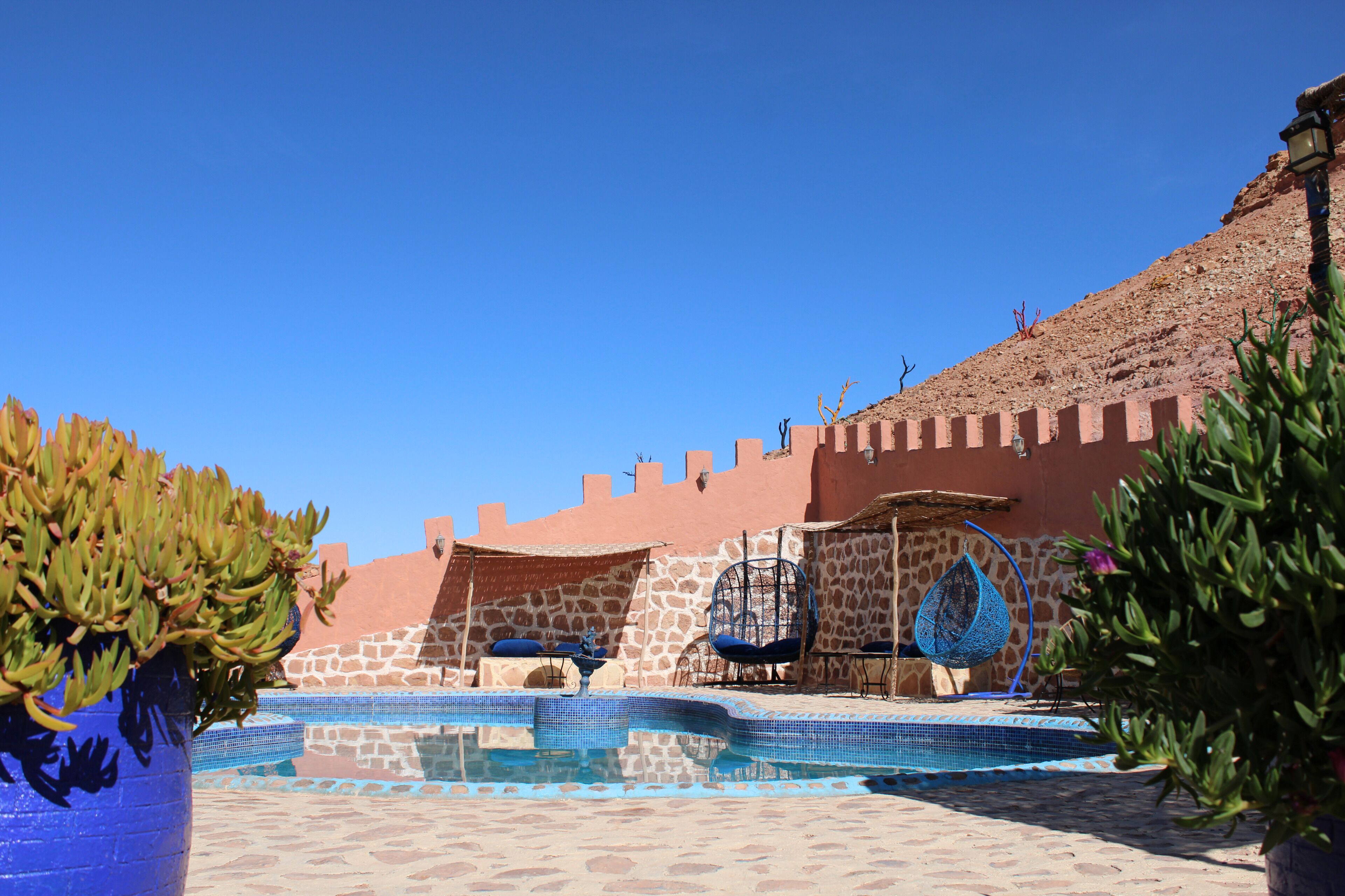 A pool area with a stone wall, hanging chairs, and a clear blue sky.