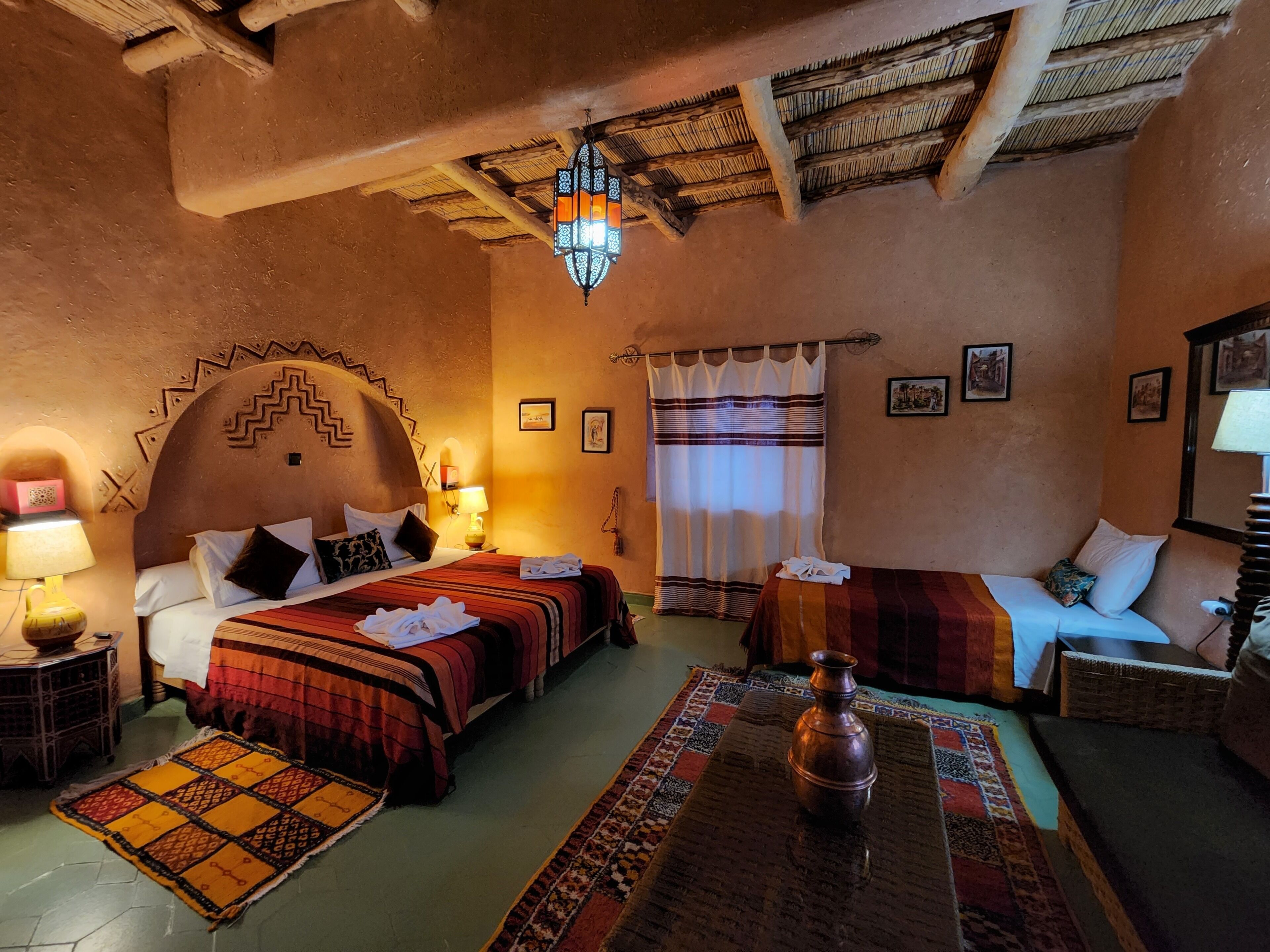 A traditional room with two beds, a sofa, a patterned rug, a hanging light fixture, and a wall-mounted mirror.