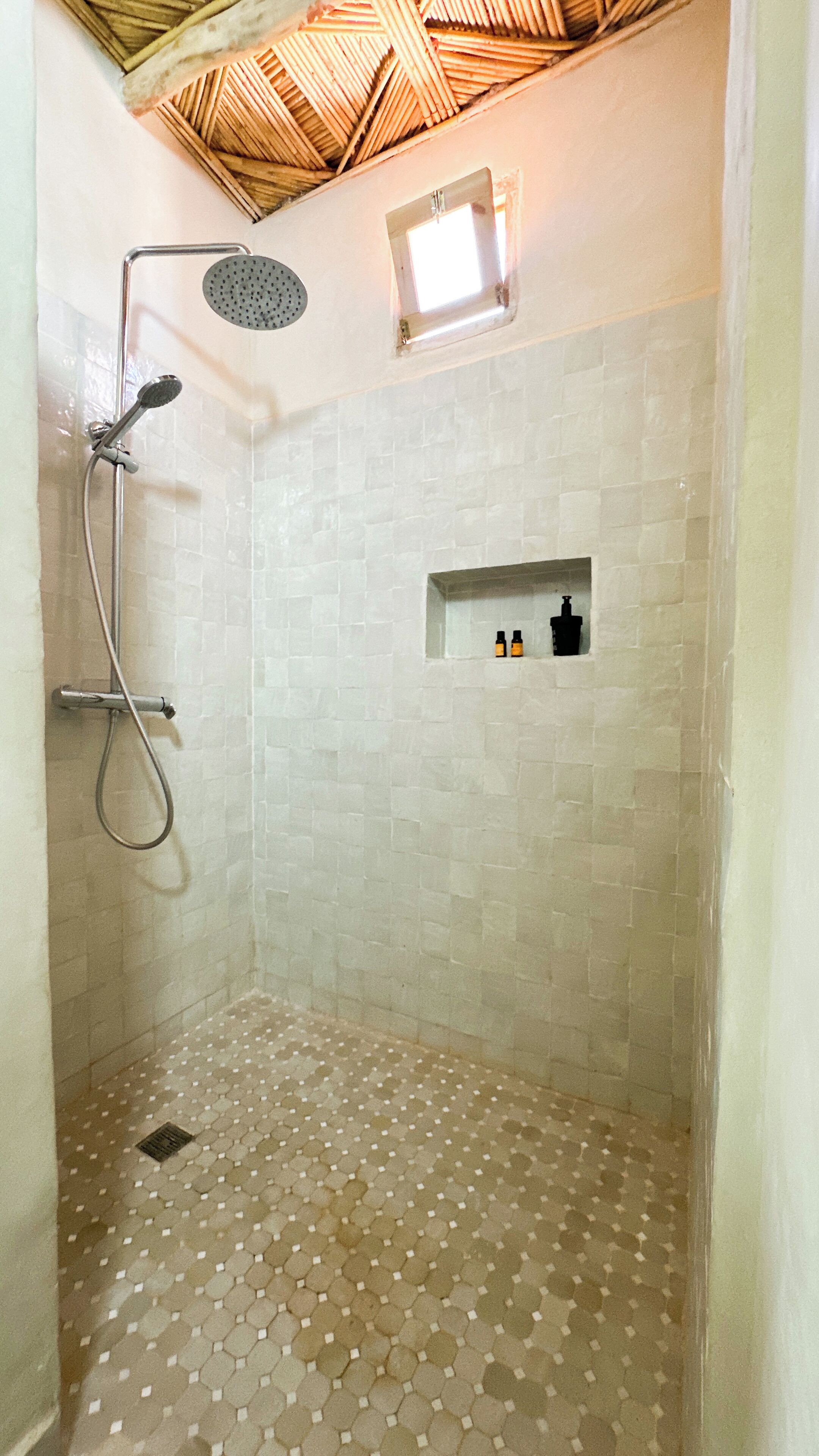 Ducha con piso de azulejos, cabezal de ducha y una pequeña ventana.
