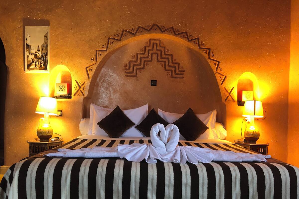 A hotel room with a large bed, striped bedding, two black pillows, and a towel arrangement.