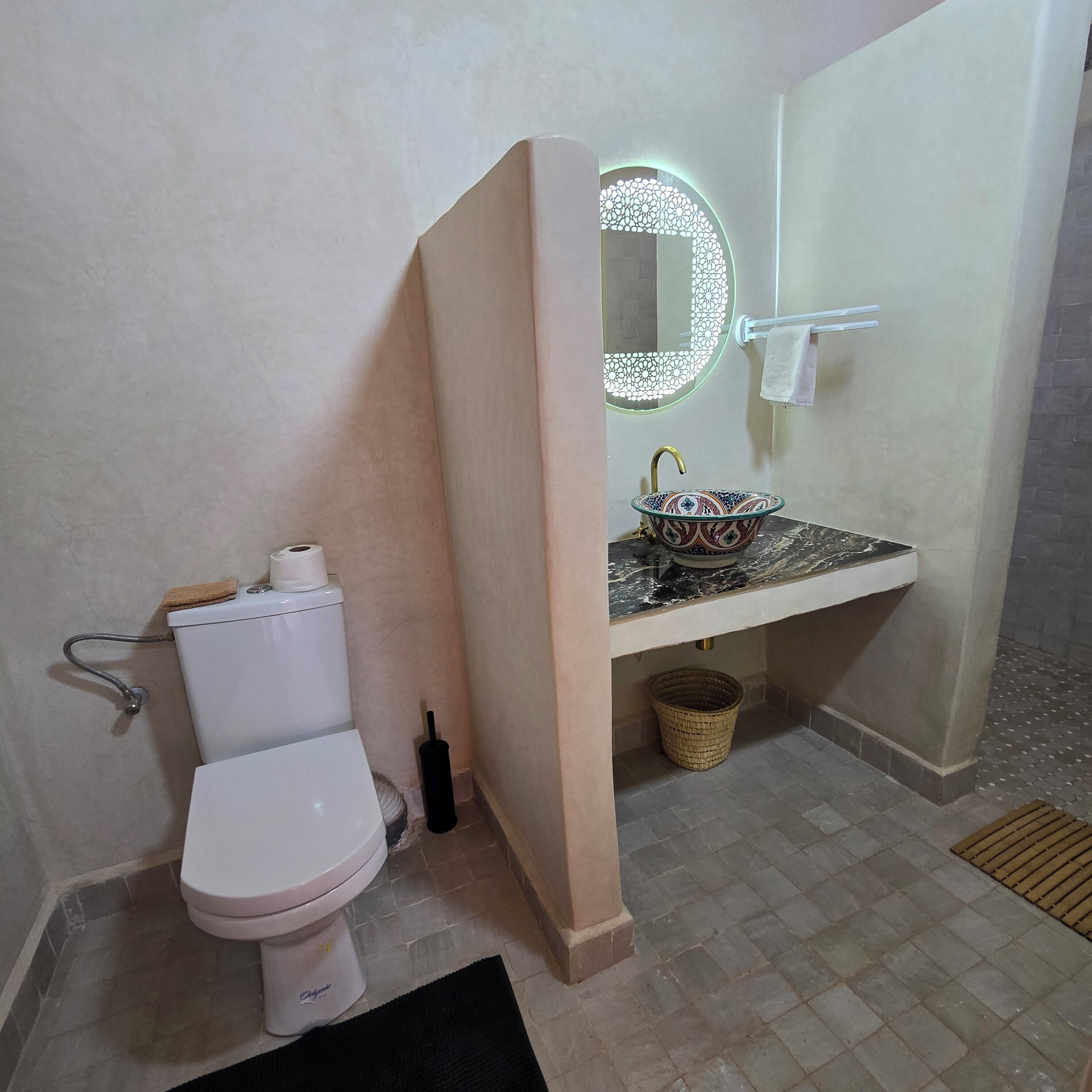 A bathroom with a toilet, a sink with a decorative basin, a mirror with a light, and a towel rack.