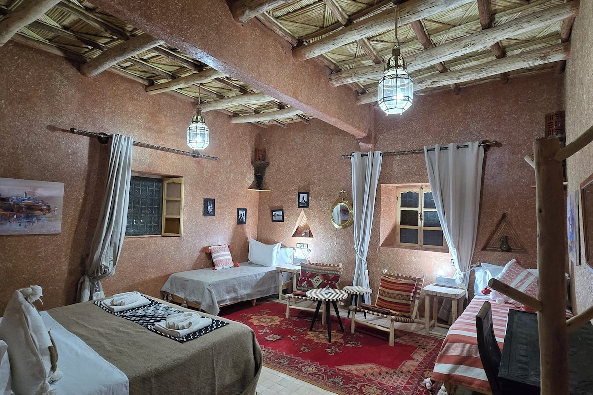 A traditional room with a high wooden ceiling, two beds, a small table, and a chair.