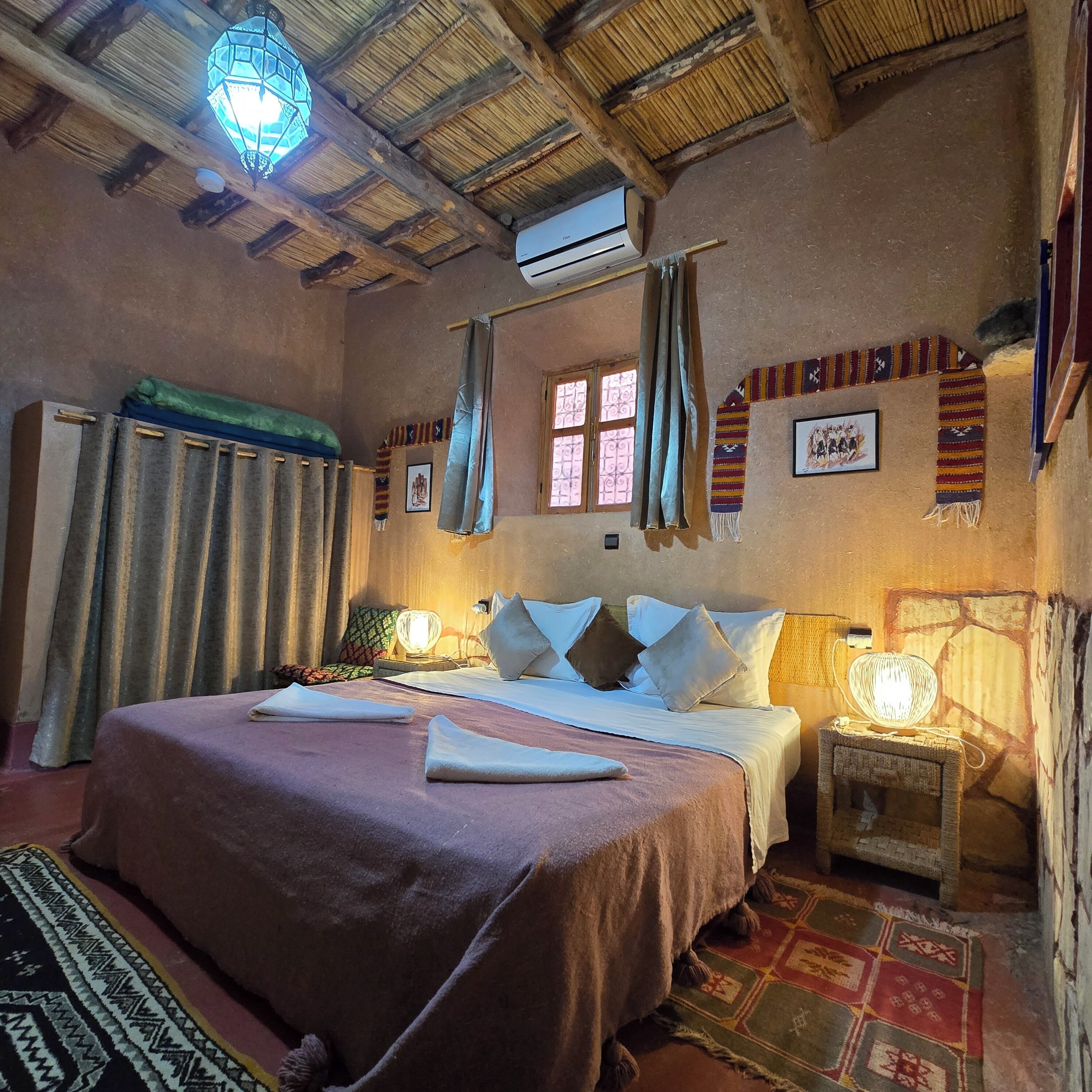A traditional room with a bed, curtains, a wall-mounted air conditioner, and a patterned rug.