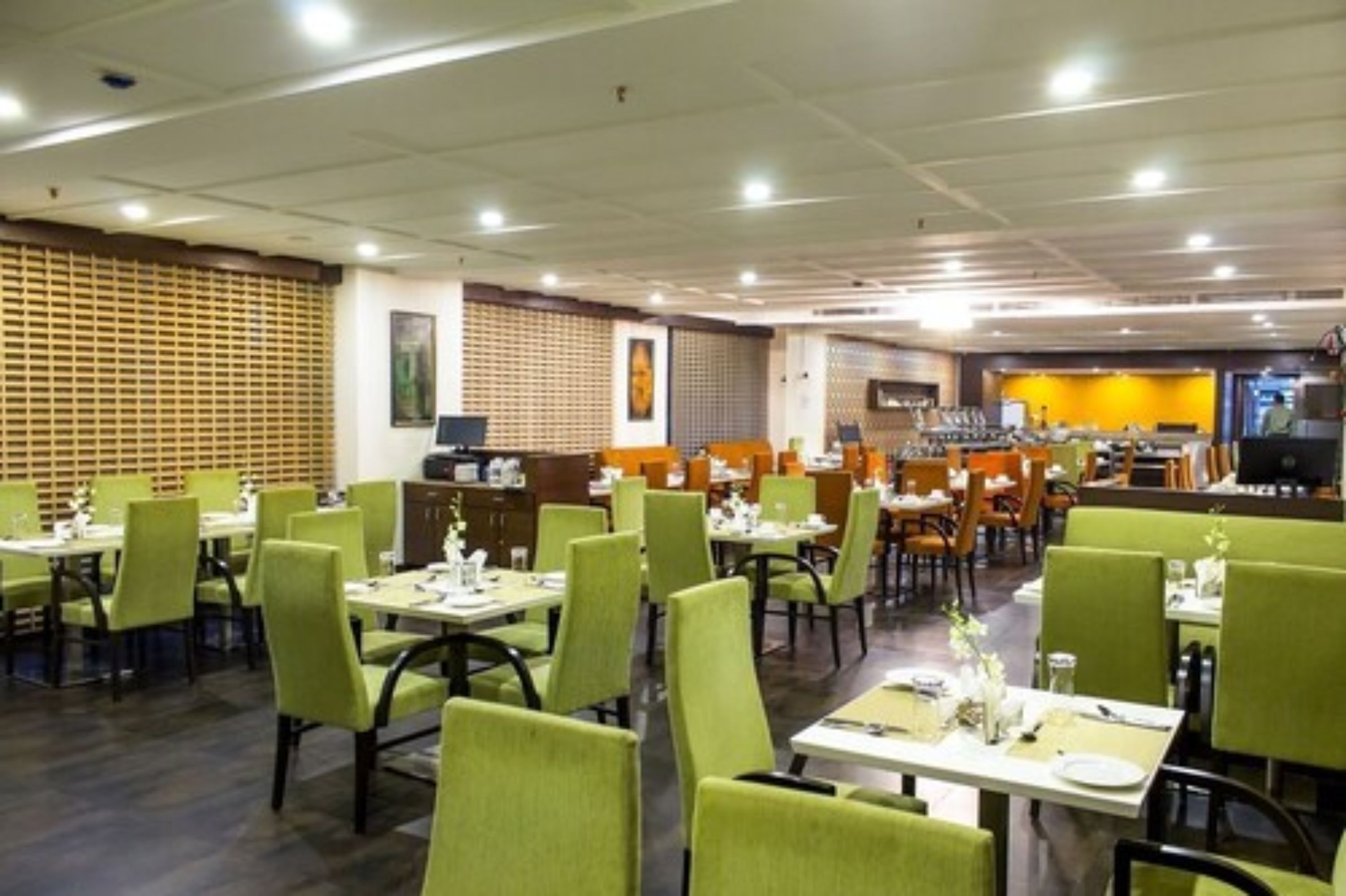 A restaurant with green chairs and tables, a wooden partition wall, and a counter area.