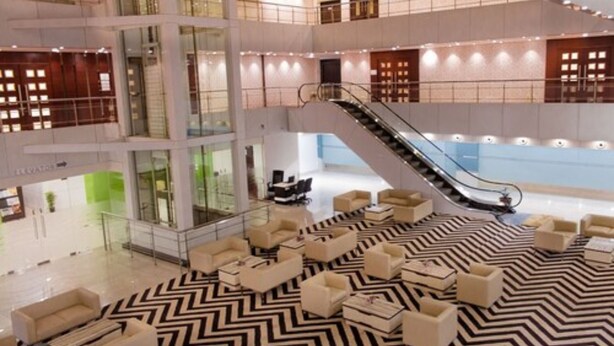Un vestíbulo amplio con una zona de estar central, una escalera y un muro de cristal al fondo.