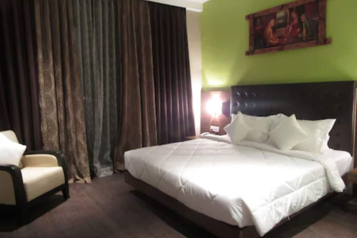 Quarto de hotel com uma cama grande, uma cadeira, um quadro na parede e uma janela com cortinas.