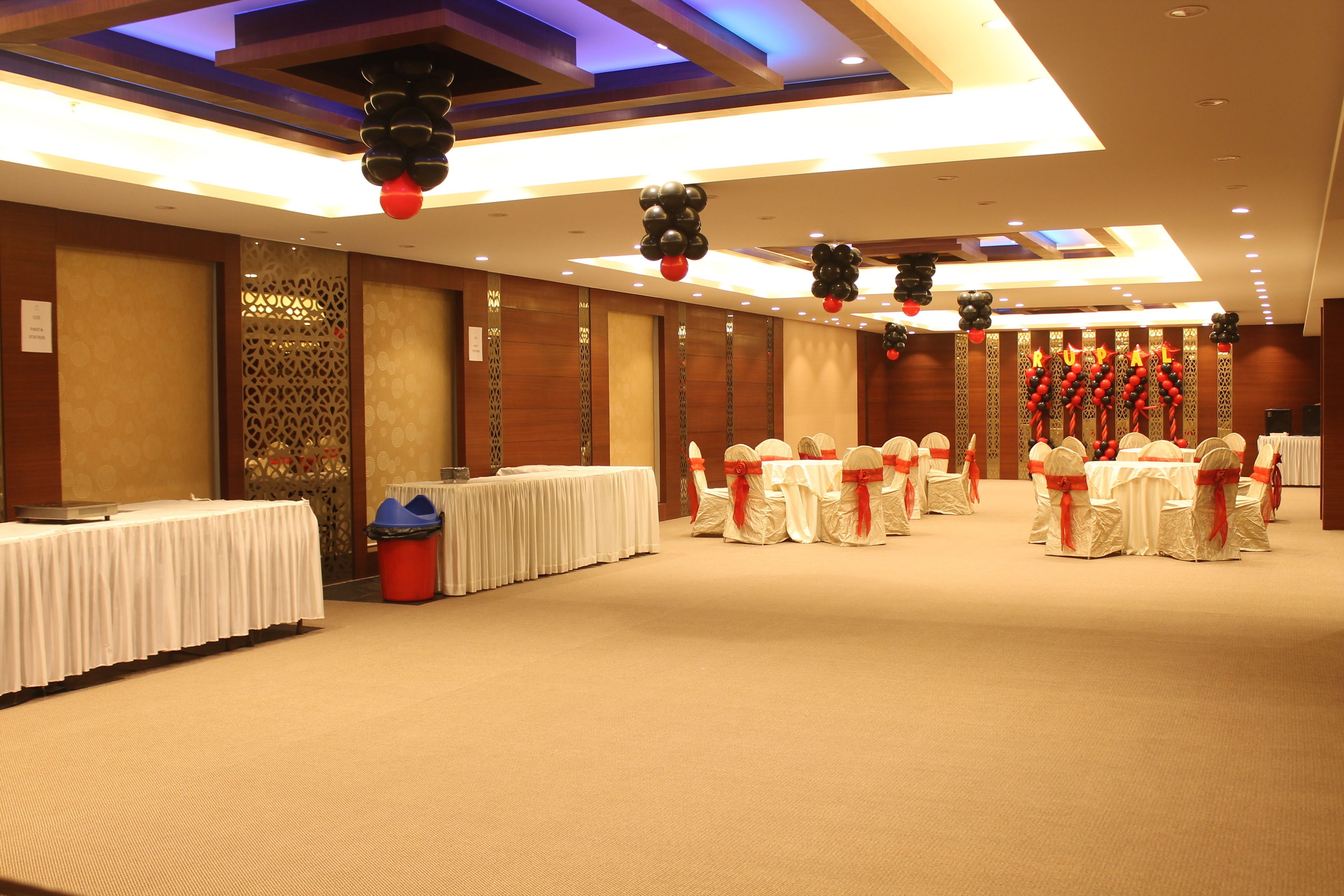 Un salón de banquetes con mesas redondas, manteles blancos y sillas con cintas rojas.