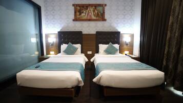 Une chambre d’hôtel avec deux lits, une grande fenêtre, un tableau au mur et une table de chevet avec une lampe.
