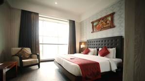 Una habitación de hotel con una cama grande, una silla, una mesa de madera y un cuadro en la pared.