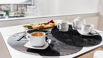 A breakfast setup with a bowl of soup, a cup of coffee, and a plate of fruit on a table with a black placemat.