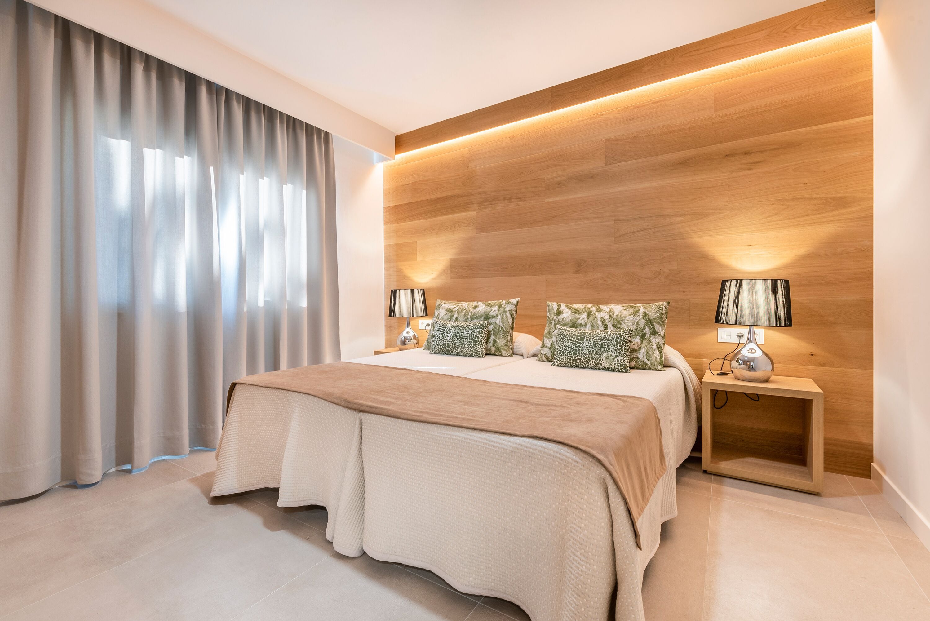 A modern bedroom with a large bed, two bedside tables with lamps, and a wooden accent wall.