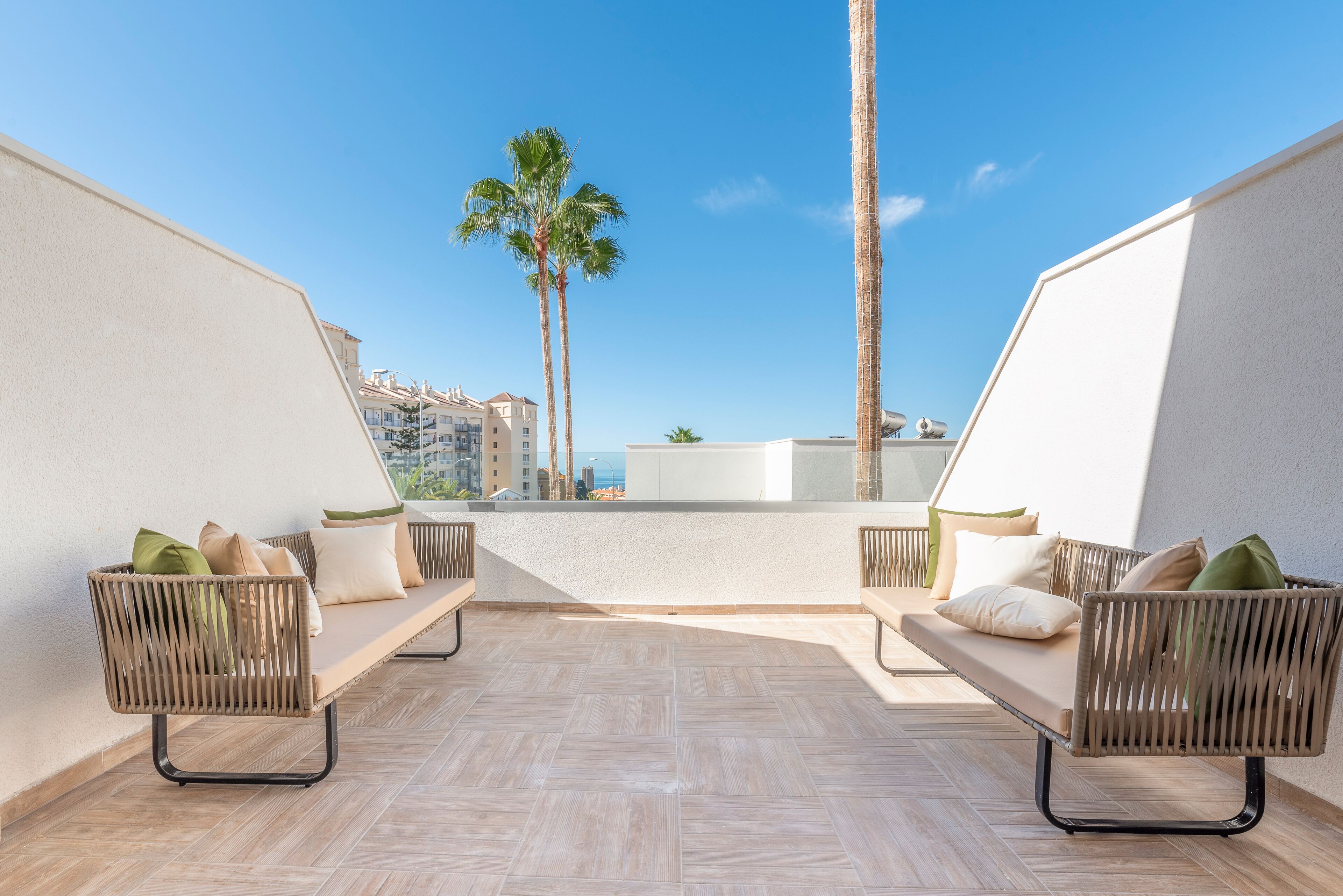 A rooftop terrace with two wicker sofas, a view of the city, and a palm tree.