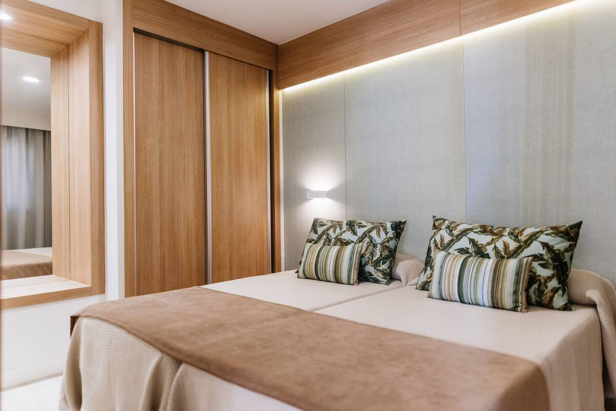 A modern hotel room with a large bed, wooden paneling, and a nightstand.