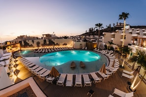 A pool area with lounge chairs and umbrellas, surrounded by buildings and palm trees. - Ohasis Boutique Suites (Arona)