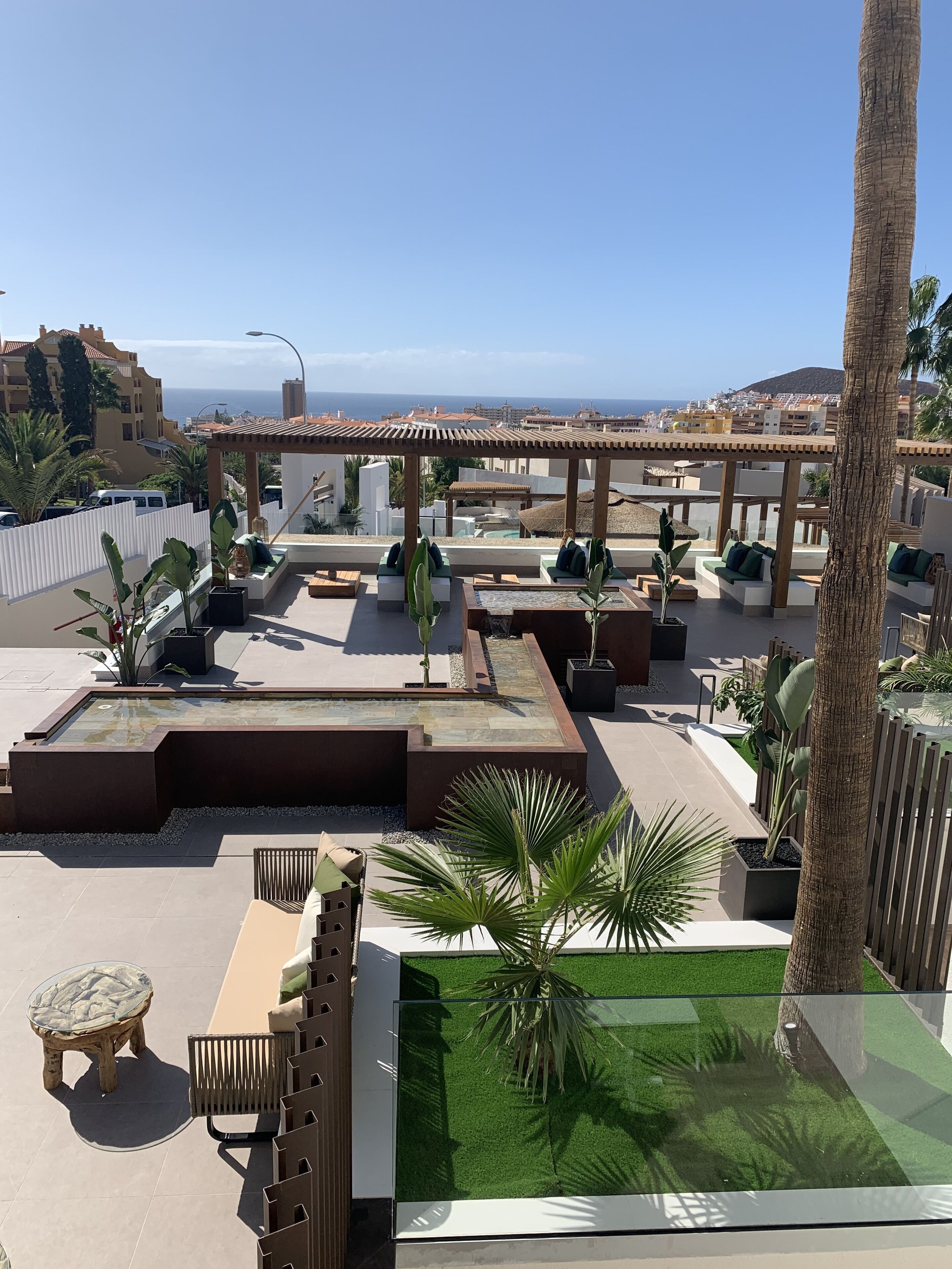 Terraza en la azotea con zonas de estar, un pequeño estanque y vistas al mar.