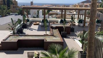 Terraza en la azotea con zonas de estar, un pequeño estanque y vistas al mar.