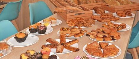 A table with various pastries and bread, arranged on plates and in wooden crates.