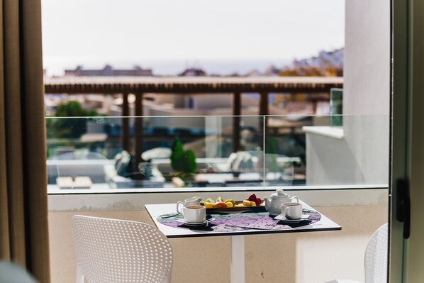 A balcony with a table set for breakfast, including a cup of coffee, fruit, and a teapot.