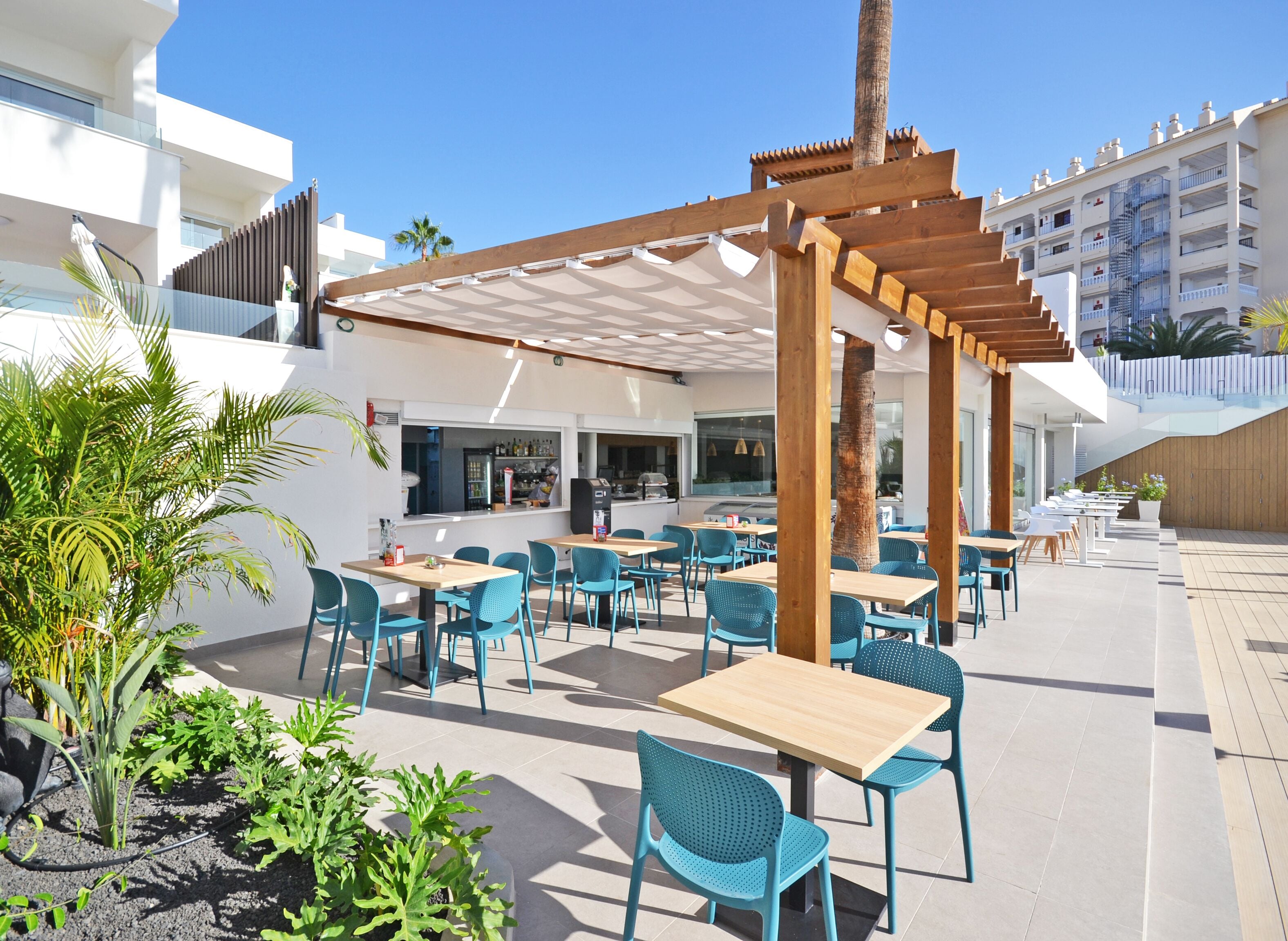 Un patio al aire libre con pérgolas de madera, sillas y mesas azules.