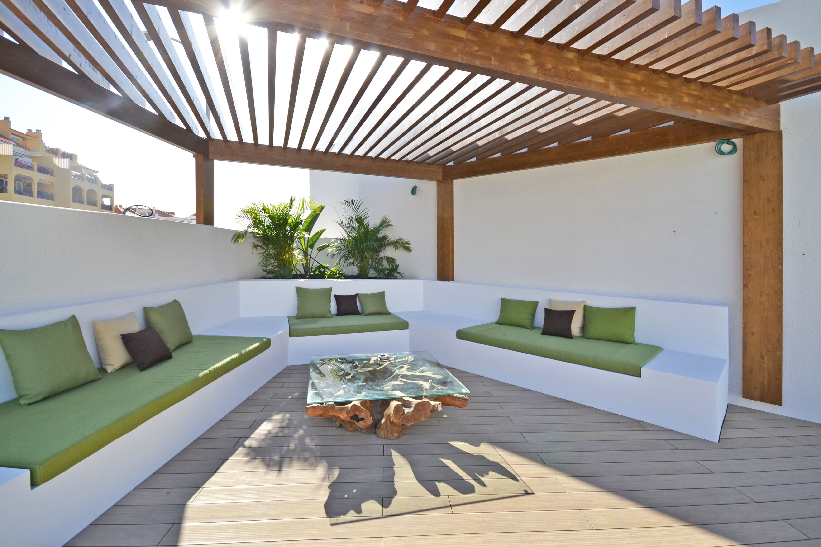 An outdoor seating area with a wooden pergola, white walls, and green cushions.