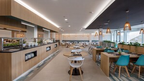 A modern cafeteria with wooden accents, round tables, and pendant lighting. - Ohasis Boutique Suites (Arona)