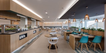 Una cafetería moderna con detalles de madera, mesas redondas e iluminación colgante.