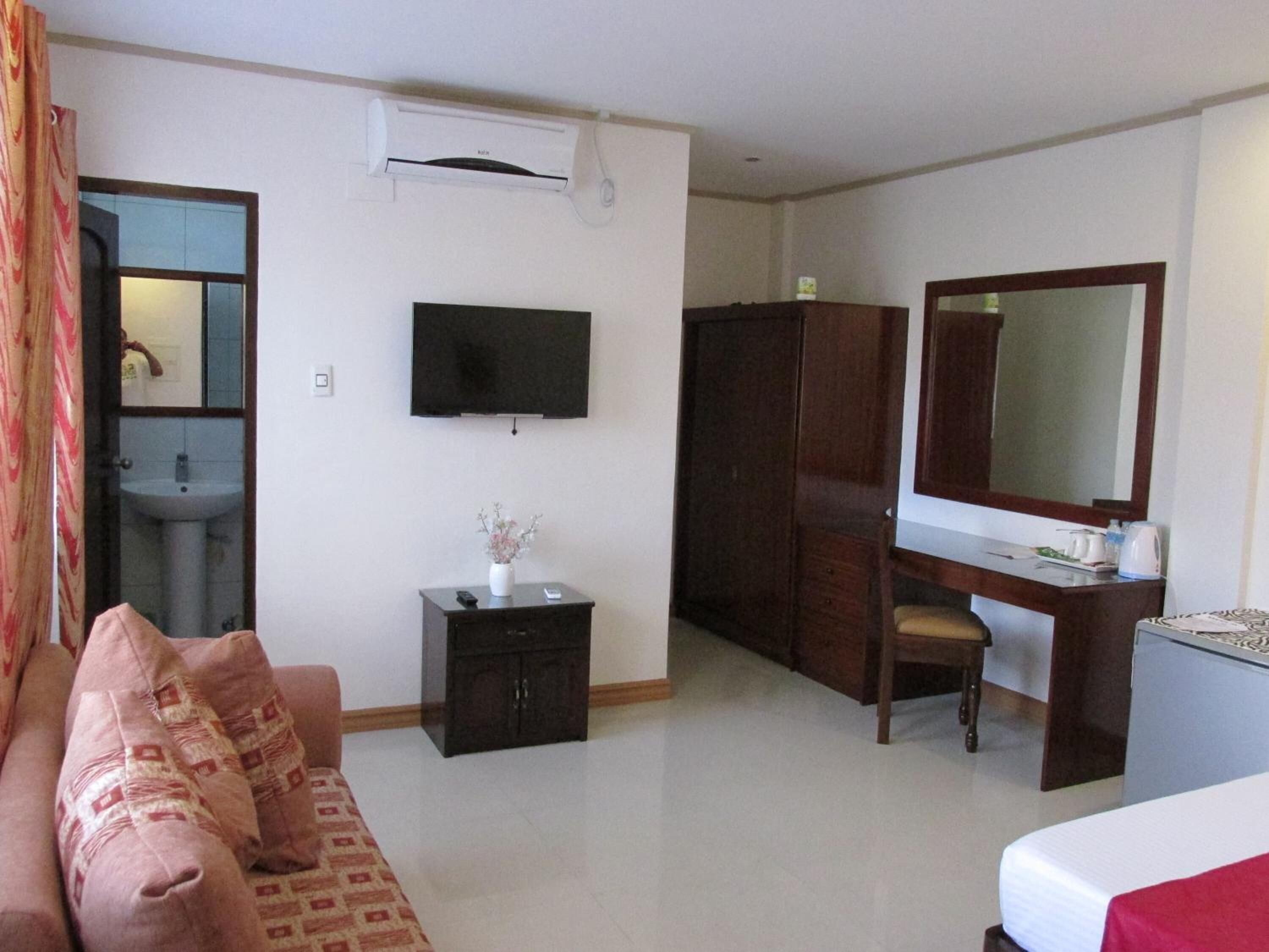 A hotel room with a sofa, a TV, a desk with a mirror, a wardrobe, and a small cabinet.