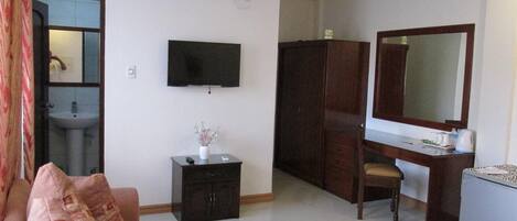 A hotel room with a sofa, a TV, a desk with a mirror, a wardrobe, and a small cabinet.