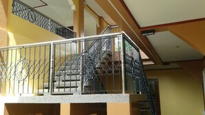 Un balcón con barandilla de hierro forjado, una escalera y una pared amarilla.