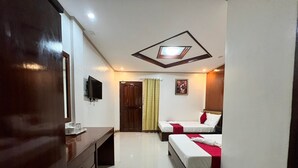 Una habitación de hotel con un escritorio de madera, un televisor de pantalla plana, dos camas con ropa de cama roja y blanca, una lámpara de techo y una puerta con cortina.
