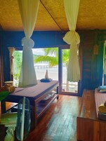 Una habitación con cama, ventilador y vista a una playa y palmeras.