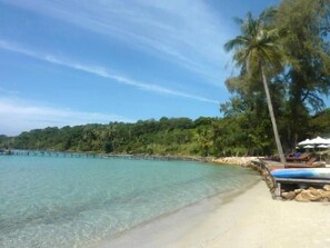 A beach with clear turquoise water, a sandy shore, and a row of palm trees. - Koh Kood Resort (Ko Kood)