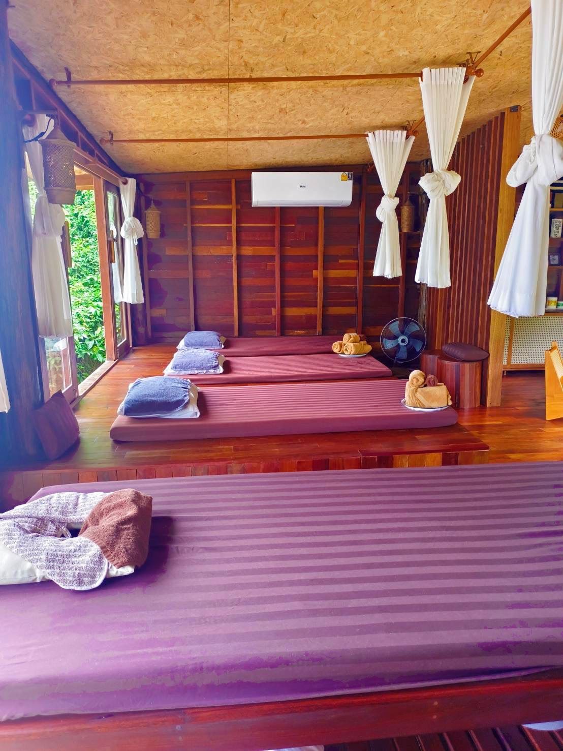 A room with two beds, a fan, and a small table with towels.