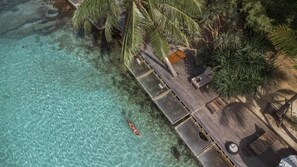 An aerial view of a beach resort with clear turquoise water, a wooden deck, palm trees, and lounge chairs. - Koh Kood Resort (Ko Kood)