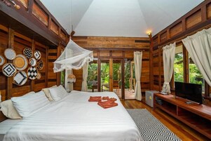 A wooden room with a bed, a TV, and a view of greenery outside.