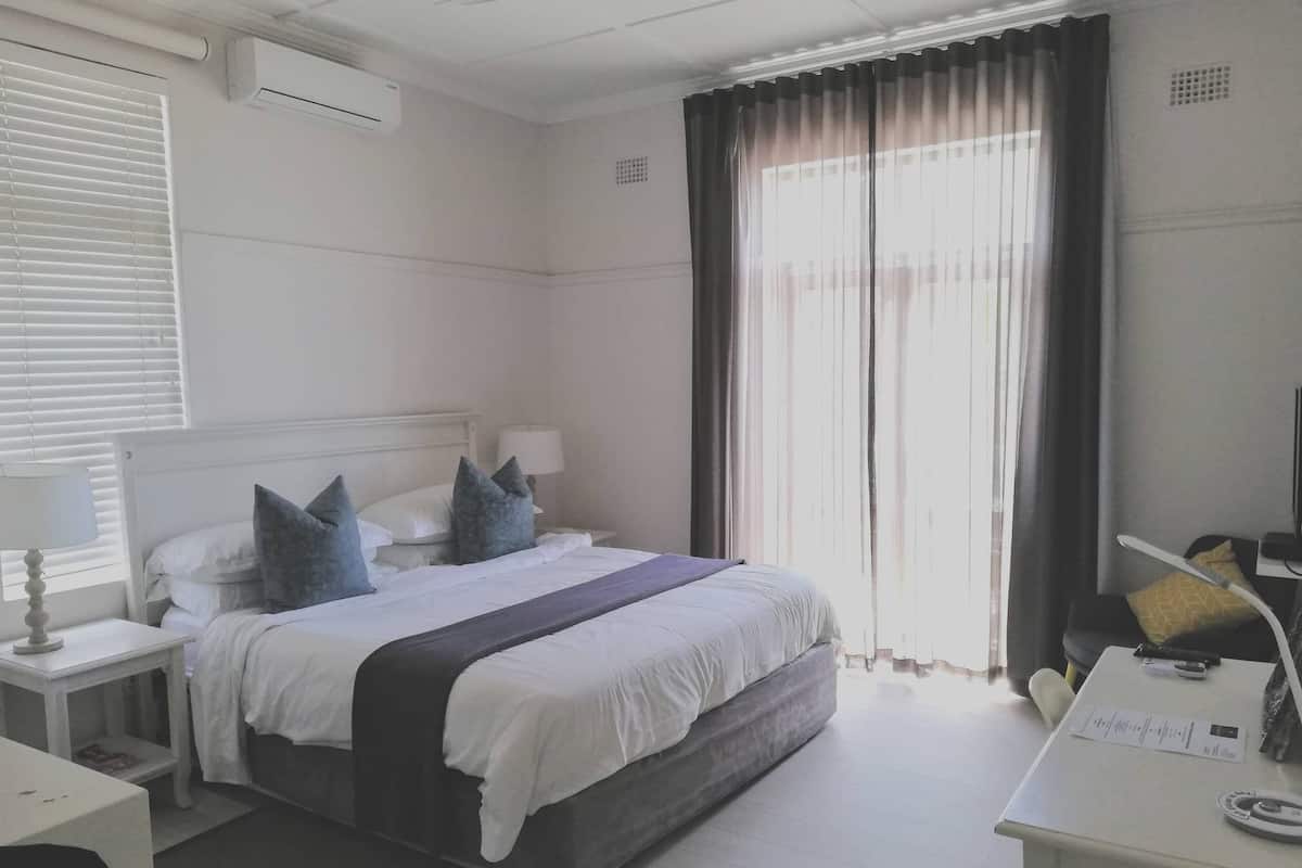 Habitación de hotel con cama, mesitas de noche, escritorio y ventana con cortinas.