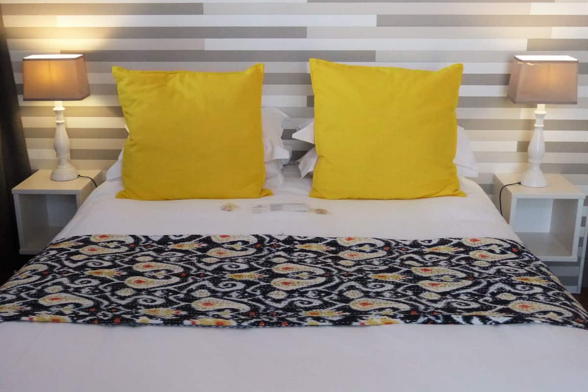 Una cama con una colcha estampada, dos almohadas amarillas brillantes y dos lámparas de noche a cada lado.