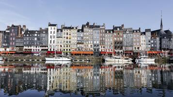 A waterfront with buildings reflecting in calm water, boats docked, and a church spire.