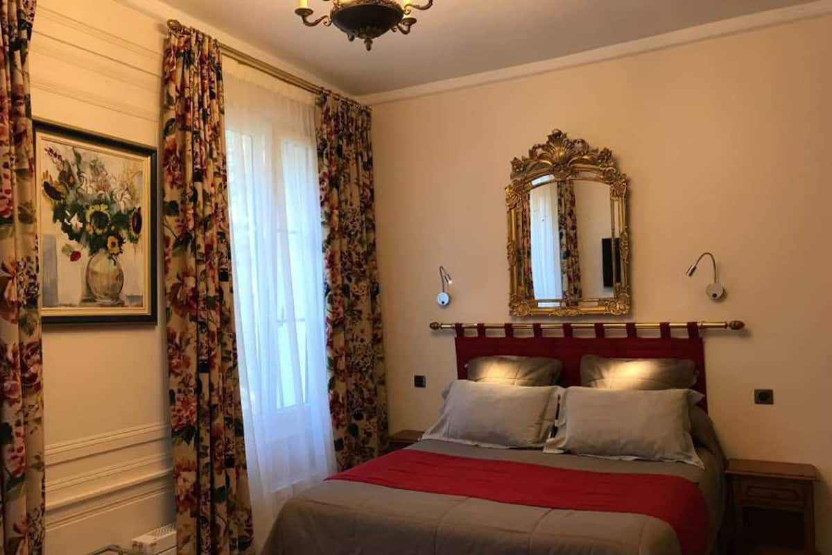 Une chambre d’hôtel avec un lit, des rideaux à motifs floraux, un grand miroir et un tableau accroché au mur.