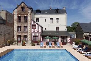 A swimming pool with lounge chairs and umbrellas, surrounded by buildings with a mix of traditional and modern architecture. - Hôtel L' Ecrin (Honfleur)