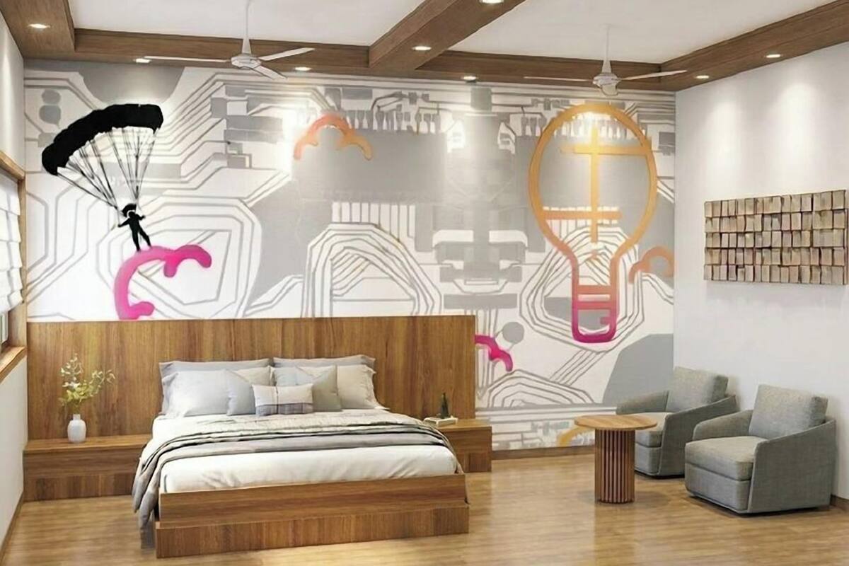 Un dormitorio moderno con cama, mesitas de noche, una zona de estar con sillas, un mural en la pared y un ventilador de techo.
