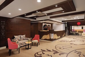 A lobby with a reception desk, a sofa, two chairs, and a patterned carpet. - Ginger Hotel Katra (Reasi)