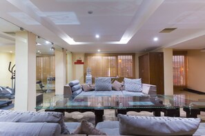 A modern living room with a glass coffee table, sofas, and a view of an exercise area.