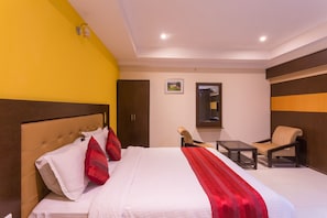 Habitación de hotel con cama, dos sillas, una mesita, un cuadro en la pared y una puerta.