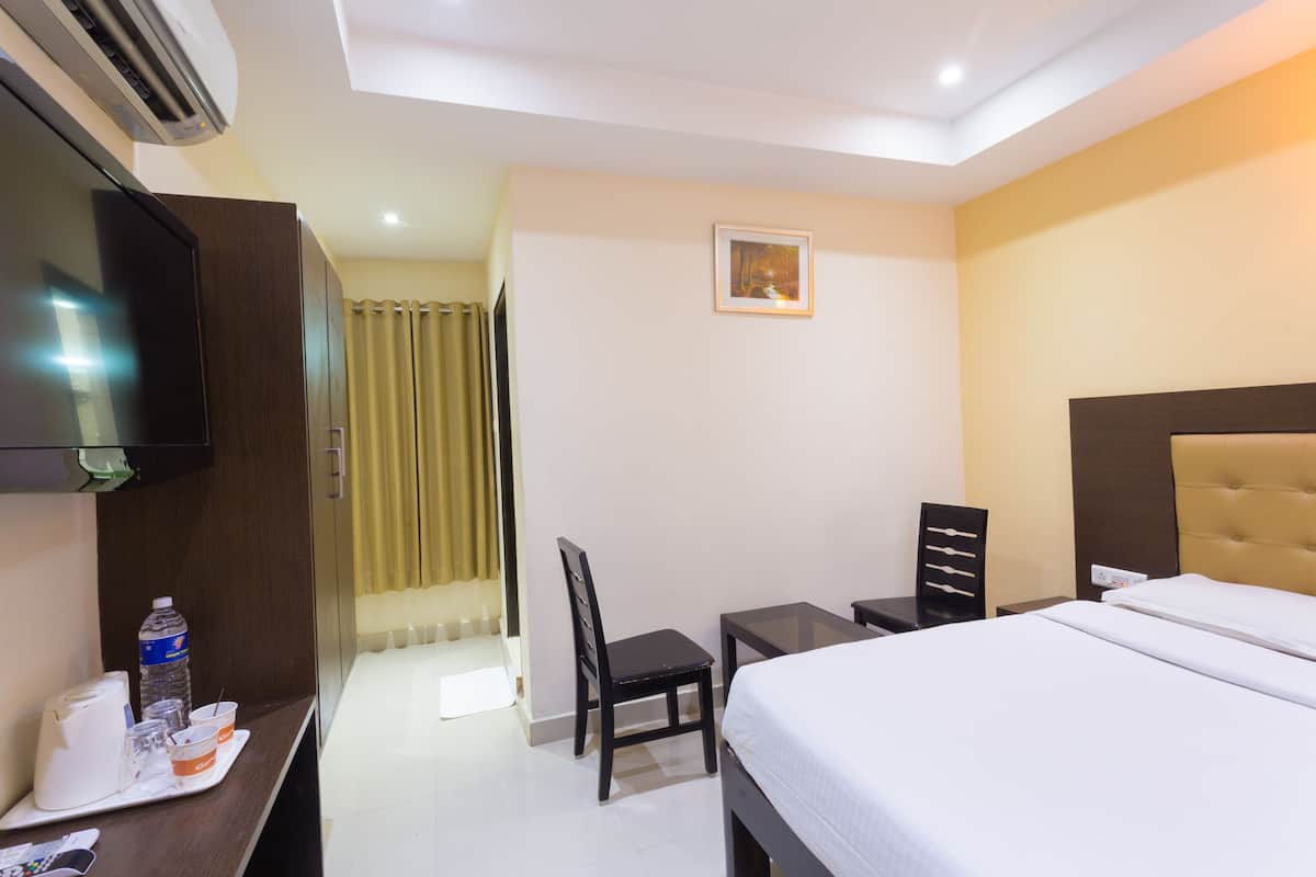 A hotel room with a bed, a desk with a chair, a television, and a window with curtains.