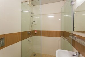 Un baño moderno con ducha envuelta en vidrio, un lavamanos blanco y una pared de acento de madera.