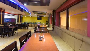 Un restaurante con una barra alargada, varias mesas y una zona de estar con bancos acolchados.