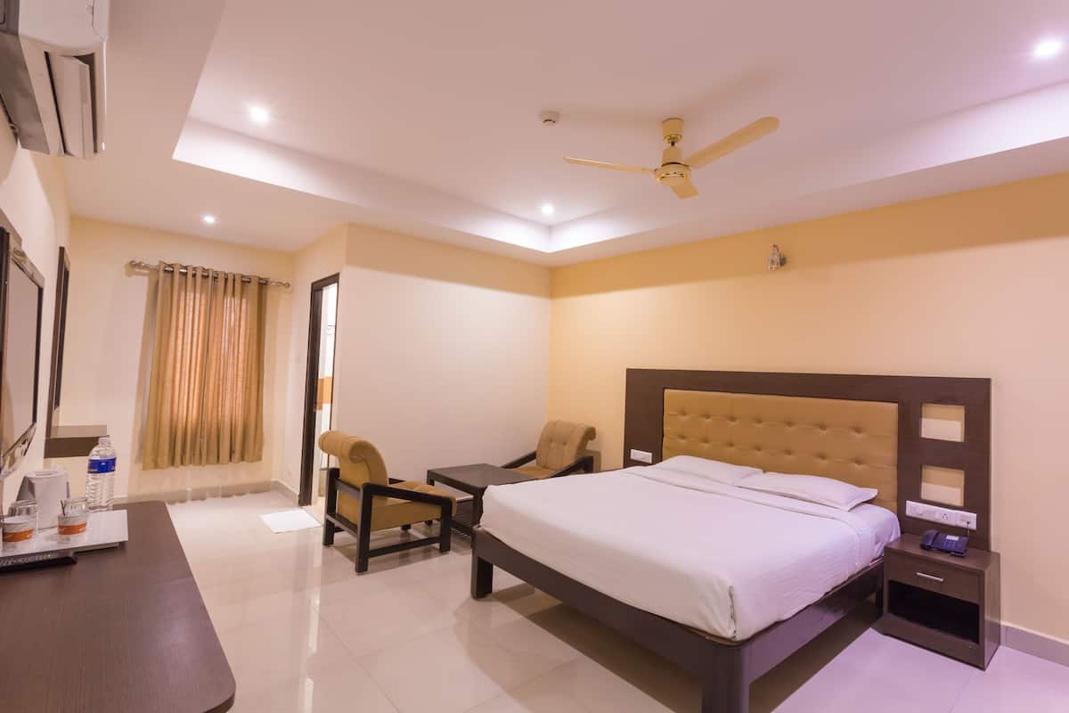 A hotel room with a bed, a desk, two chairs, a nightstand, a ceiling fan, and a window with curtains.