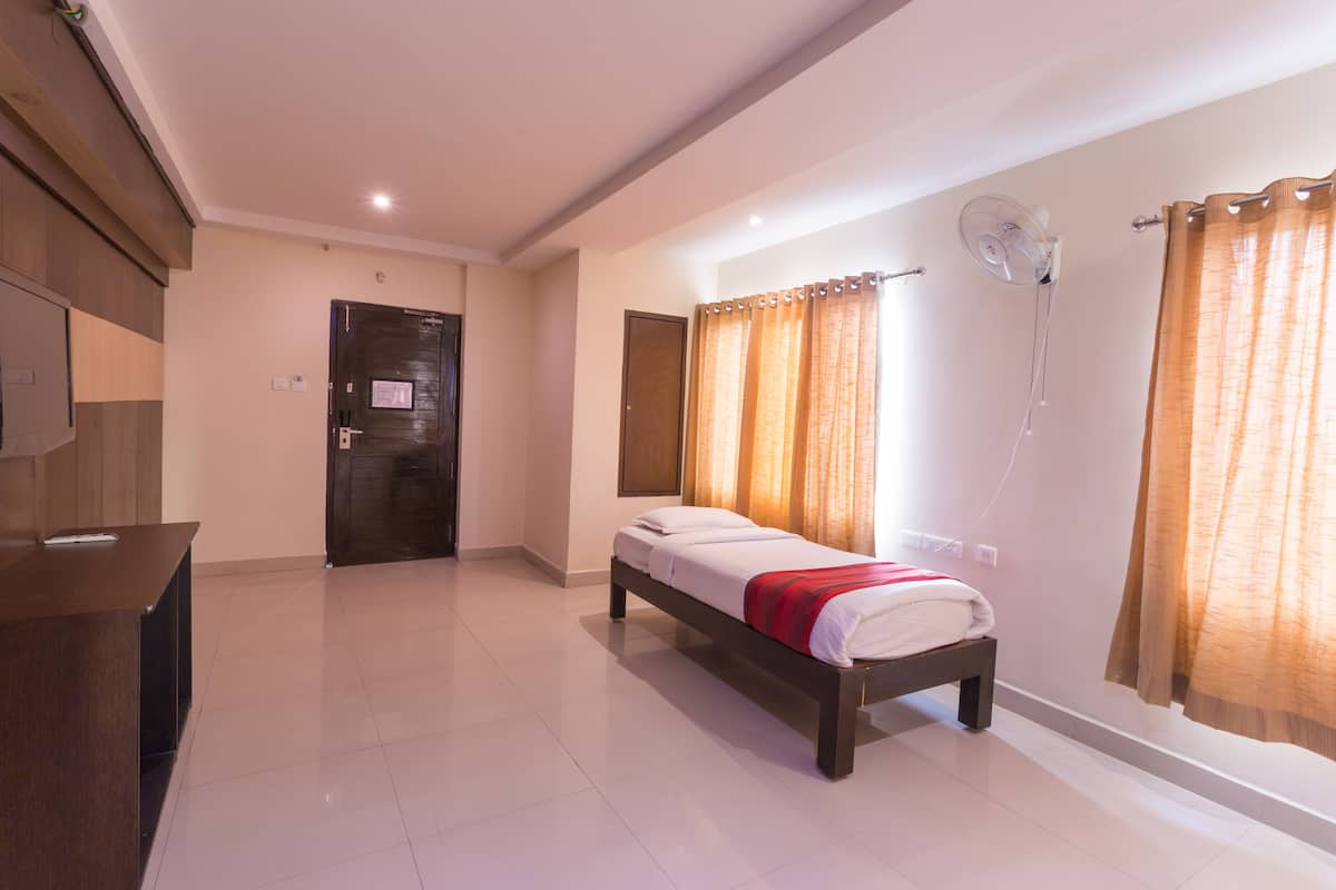 A hotel room with a bed, a desk, a fan, and curtains.