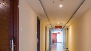 Un pasillo de hotel con una puerta de madera a la izquierda, suelo de baldosas y un letrero rojo encima.